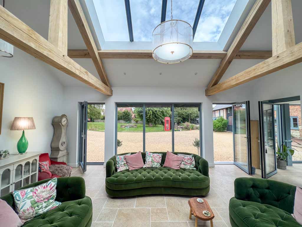 Open plan living and dining area featuring a wooden dining table with chairs, a comfortable sofa, and large windows overlooking a garden. The room is decorated in neutral tones, creating a relaxed and homely environment.